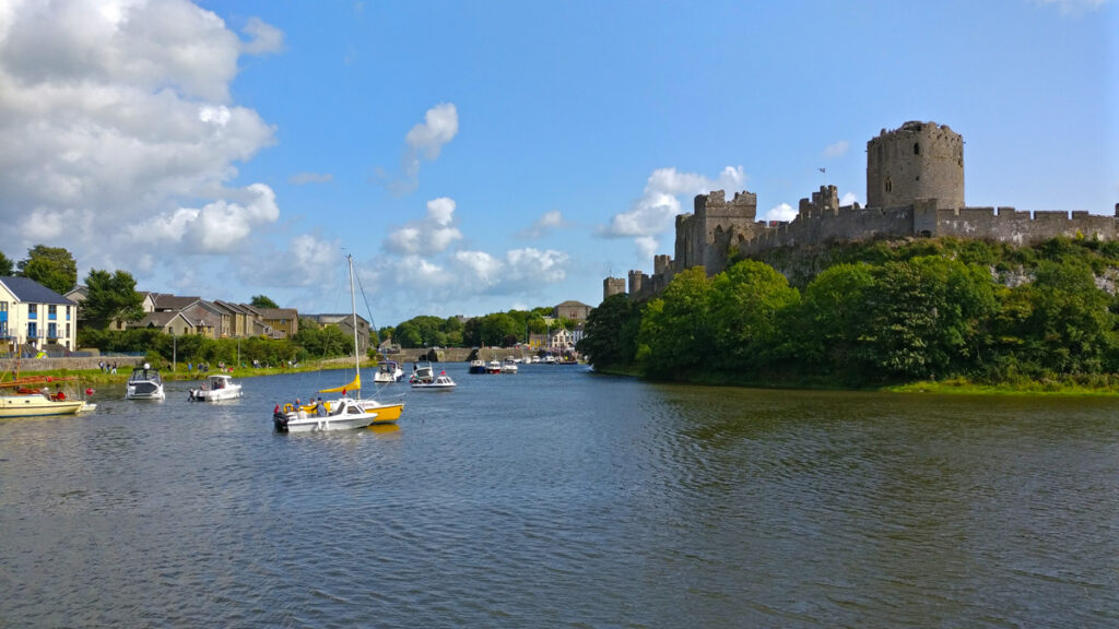 The Castle pond from the perspectie of the barage with multiple boats of various colours floating in the water.
blue skies and white clouds overhead.